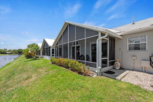 back of house with a lawn, a sunroom, a water view, and stucco siding