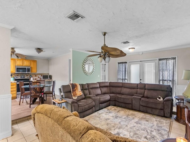 living room featuring ceiling fan, a textured ceiling, ornamental molding, and light tile patterned flooring