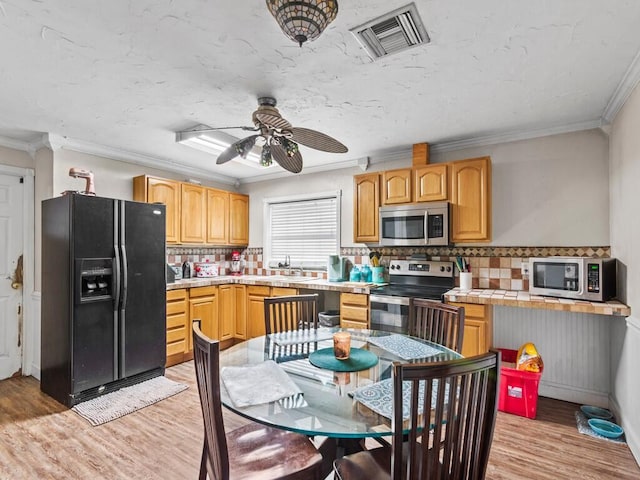 kitchen featuring tasteful backsplash, ceiling fan, light hardwood / wood-style flooring, appliances with stainless steel finishes, and ornamental molding