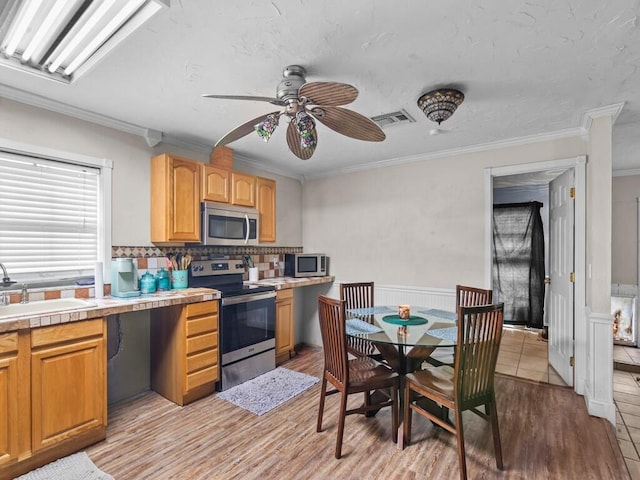 kitchen featuring appliances with stainless steel finishes, decorative backsplash, sink, light hardwood / wood-style flooring, and crown molding