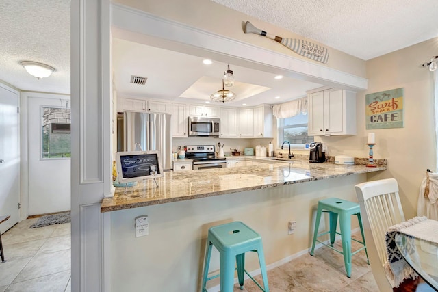 kitchen featuring stainless steel appliances, white cabinetry, a sink, a peninsula, and a kitchen bar