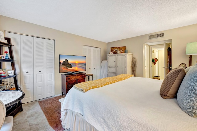 bedroom featuring a textured ceiling, light tile patterned flooring, visible vents, and multiple closets