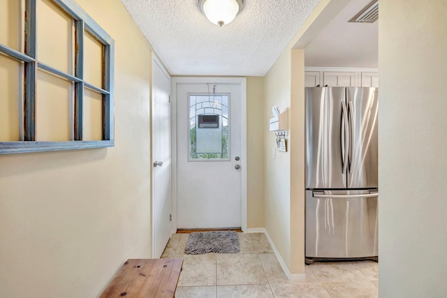 doorway with light tile patterned floors, baseboards, visible vents, and a textured ceiling