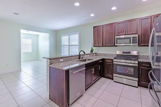 kitchen with light stone countertops, stainless steel appliances, sink, kitchen peninsula, and light tile patterned floors