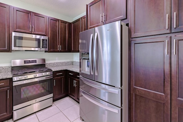 kitchen featuring light tile patterned floors, appliances with stainless steel finishes, light stone counters, and a textured ceiling