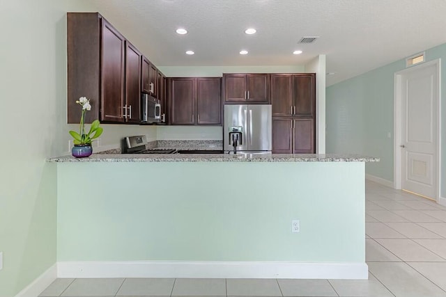 kitchen featuring light tile patterned floors, kitchen peninsula, stainless steel appliances, light stone counters, and dark brown cabinetry