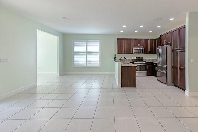 kitchen with recessed lighting, appliances with stainless steel finishes, open floor plan, light stone counters, and light tile patterned flooring