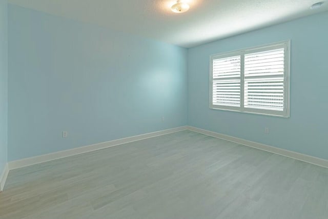 empty room featuring light wood-type flooring, baseboards, and a textured ceiling