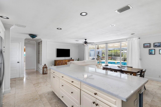 kitchen featuring ceiling fan, light stone countertops, crown molding, and a kitchen island