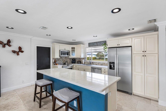 kitchen with appliances with stainless steel finishes, a kitchen bar, decorative backsplash, ornamental molding, and light stone counters