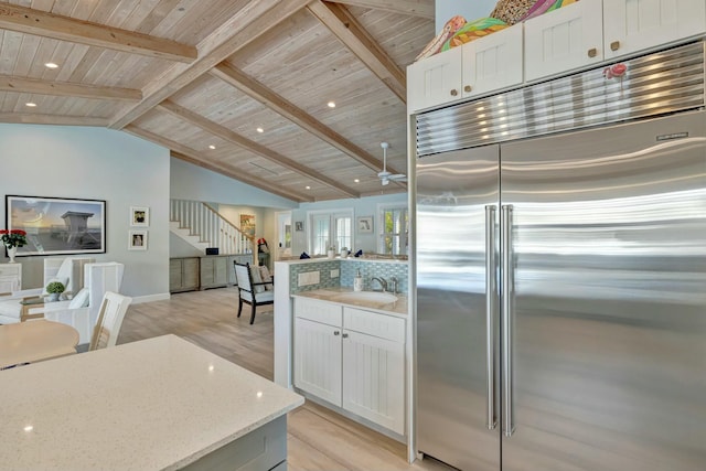 kitchen featuring vaulted ceiling with beams, built in fridge, white cabinets, and light stone countertops