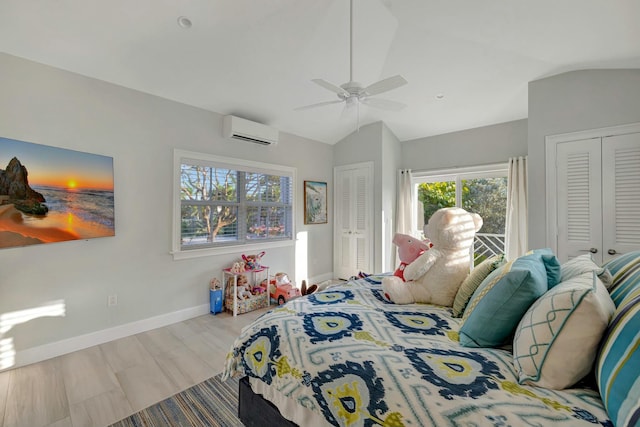 bedroom with ceiling fan, vaulted ceiling, a wall unit AC, and multiple closets