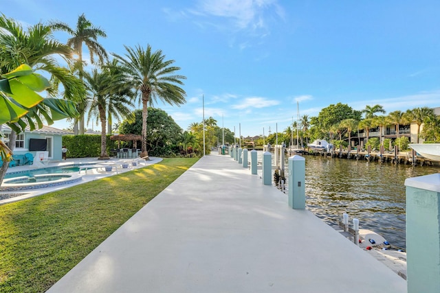 dock area with a water view, a lawn, and an in ground hot tub