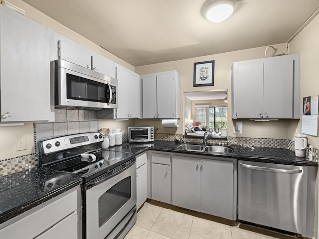 kitchen with stainless steel appliances, sink, dark stone counters, and light tile patterned floors