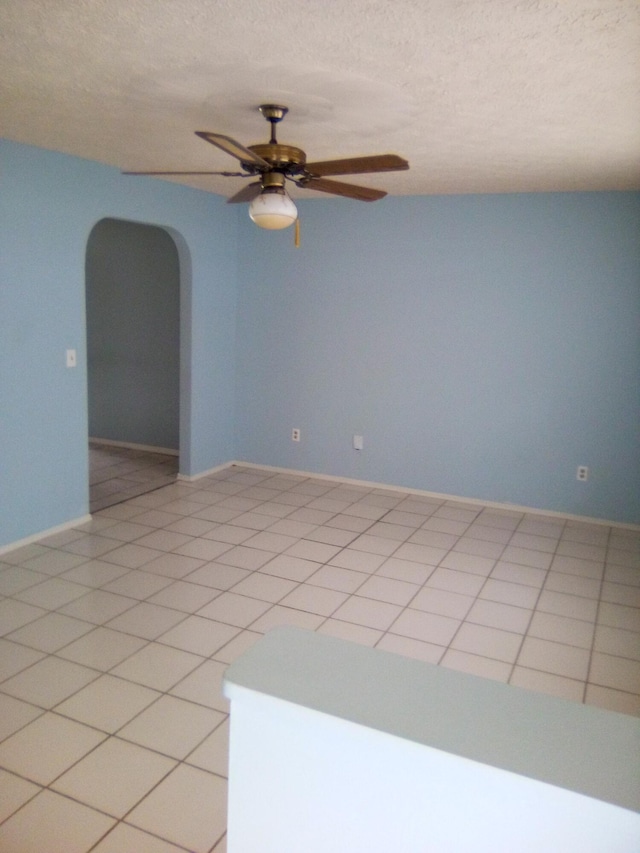 empty room featuring a textured ceiling, ceiling fan, and light tile patterned flooring