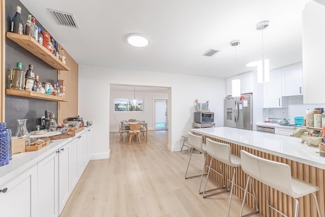 kitchen featuring a kitchen bar, white cabinetry, hanging light fixtures, light hardwood / wood-style flooring, and appliances with stainless steel finishes