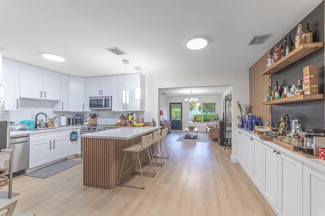 kitchen with a breakfast bar area, white cabinetry, hanging light fixtures, stainless steel appliances, and light hardwood / wood-style floors