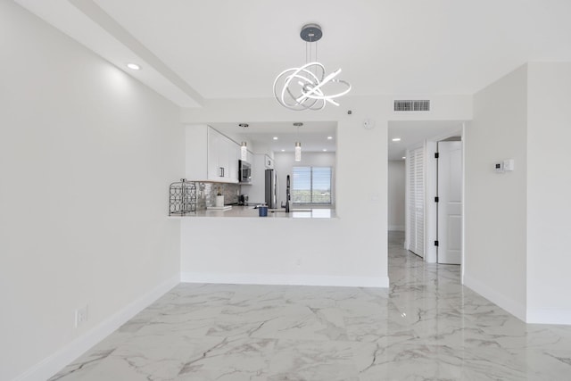 interior space with decorative light fixtures, backsplash, kitchen peninsula, an inviting chandelier, and white cabinets