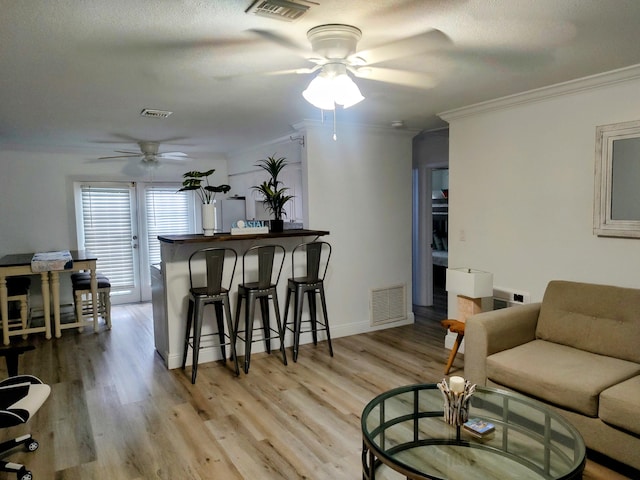 living room featuring ceiling fan, a textured ceiling, light hardwood / wood-style flooring, and ornamental molding