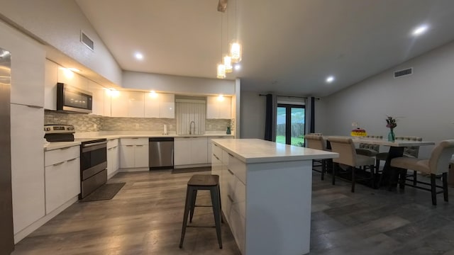 kitchen with white cabinetry, tasteful backsplash, decorative light fixtures, vaulted ceiling, and stainless steel appliances