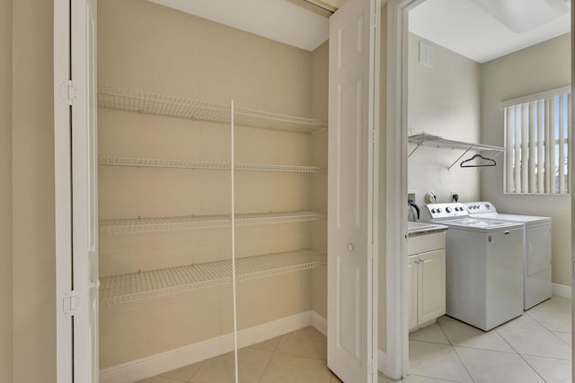 clothes washing area with washing machine and dryer, cabinets, and light tile patterned floors