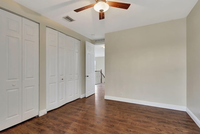 unfurnished bedroom with dark wood-type flooring, ceiling fan, and two closets