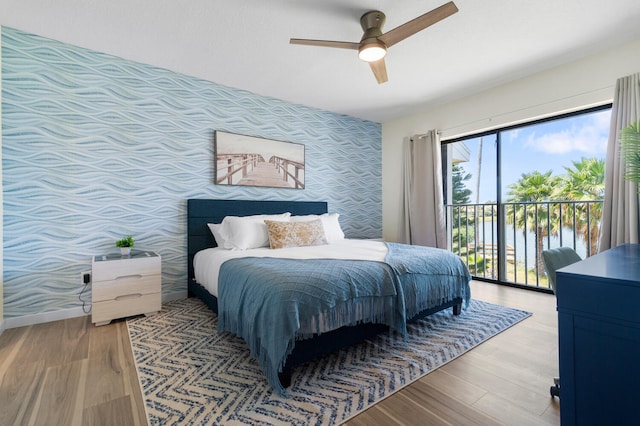 bedroom featuring a water view, light hardwood / wood-style flooring, access to exterior, and ceiling fan