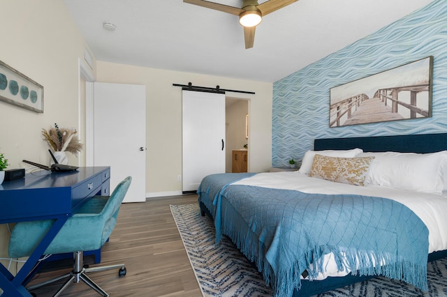 bedroom featuring ceiling fan, a barn door, dark wood-type flooring, and connected bathroom