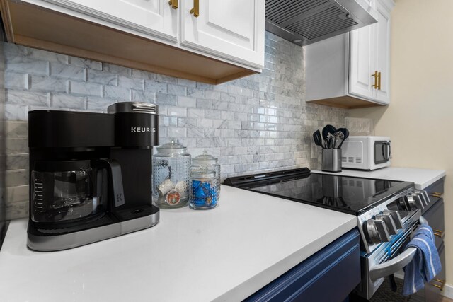 kitchen with tasteful backsplash, white cabinets, stainless steel electric range oven, and wall chimney range hood