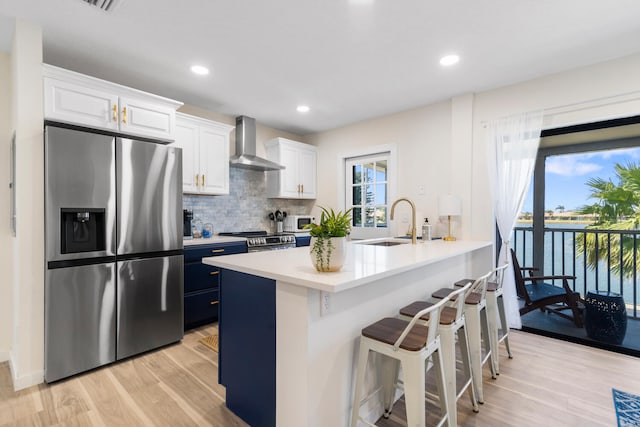 kitchen with a kitchen breakfast bar, appliances with stainless steel finishes, wall chimney range hood, and white cabinetry