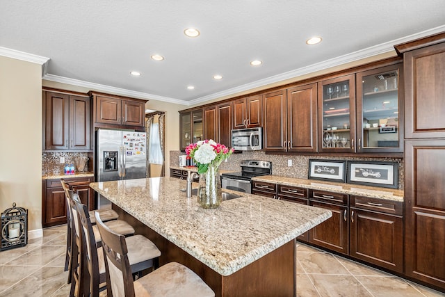 kitchen featuring dark brown cabinetry, stainless steel appliances, tasteful backsplash, an island with sink, and light stone counters