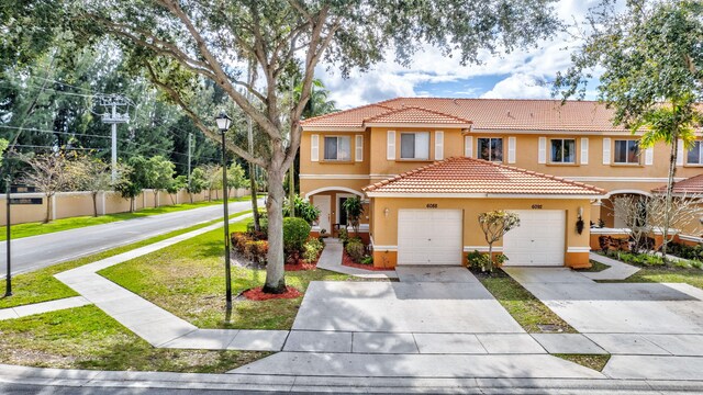 view of front facade featuring driveway, a tiled roof, an attached garage, fence, and stucco siding