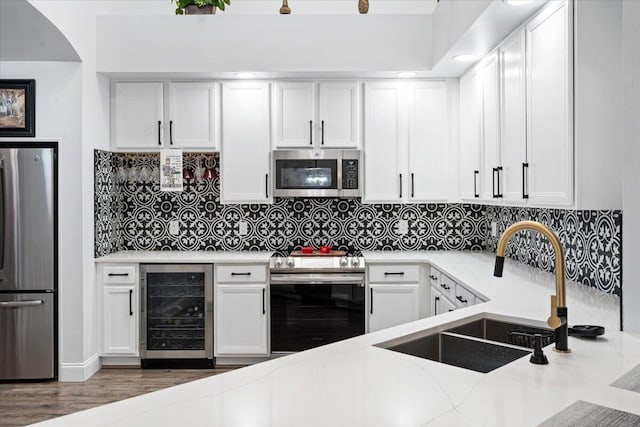 kitchen with sink, appliances with stainless steel finishes, beverage cooler, decorative backsplash, and white cabinets