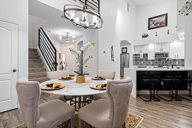 dining room with an inviting chandelier, a towering ceiling, sink, and light hardwood / wood-style floors