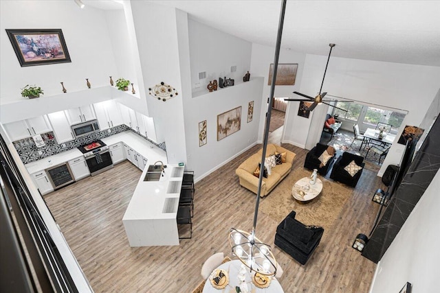 living room featuring ceiling fan, sink, high vaulted ceiling, and light wood-type flooring