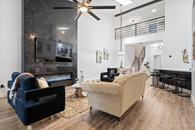 living room featuring a high end fireplace, wood-type flooring, ceiling fan, and a high ceiling