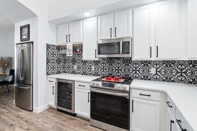 kitchen with appliances with stainless steel finishes, light stone countertops, light hardwood / wood-style floors, white cabinets, and beverage cooler