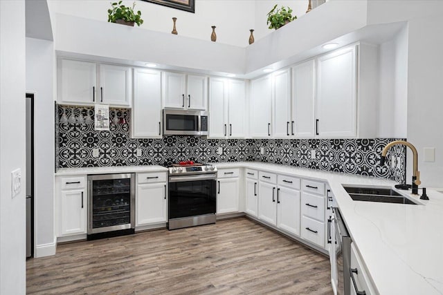 kitchen with sink, appliances with stainless steel finishes, white cabinetry, wine cooler, and light stone countertops