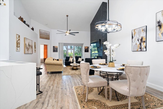 dining room featuring hardwood / wood-style flooring, ceiling fan with notable chandelier, and high vaulted ceiling