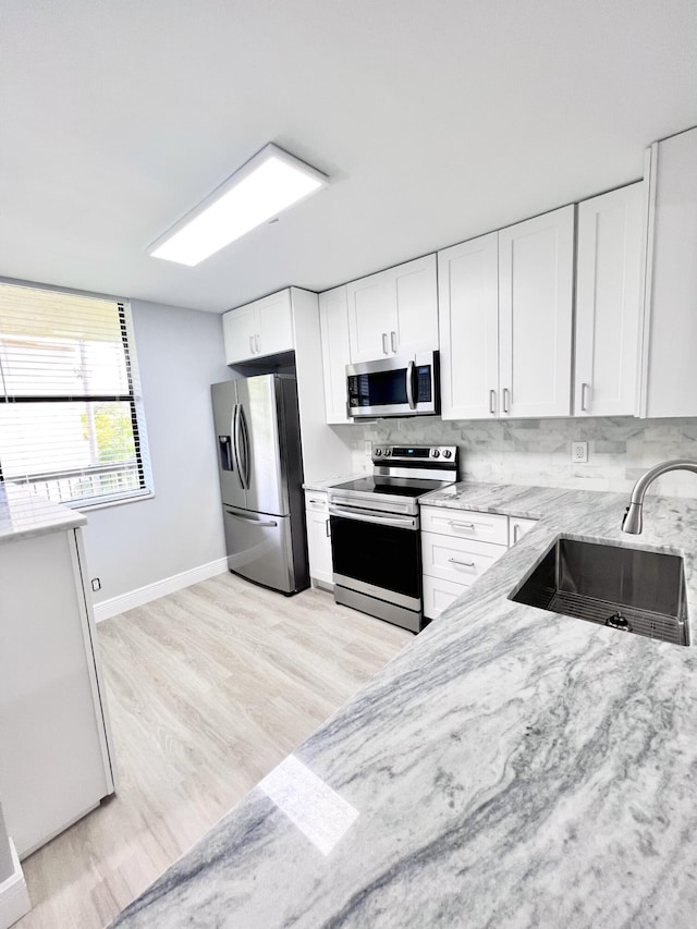 kitchen with appliances with stainless steel finishes, white cabinetry, tasteful backsplash, and sink