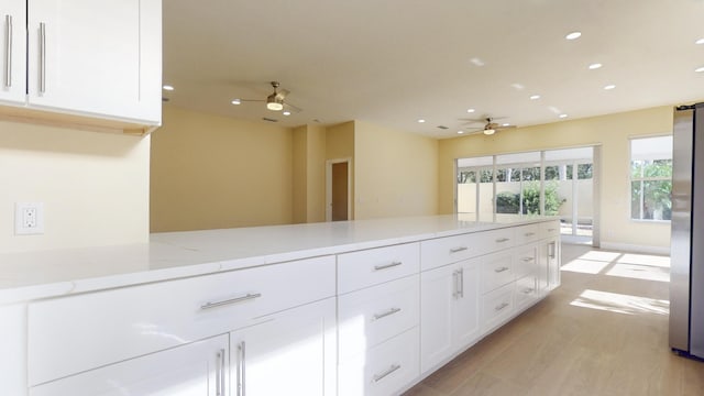 kitchen featuring light stone counters, stainless steel fridge, white cabinets, and ceiling fan