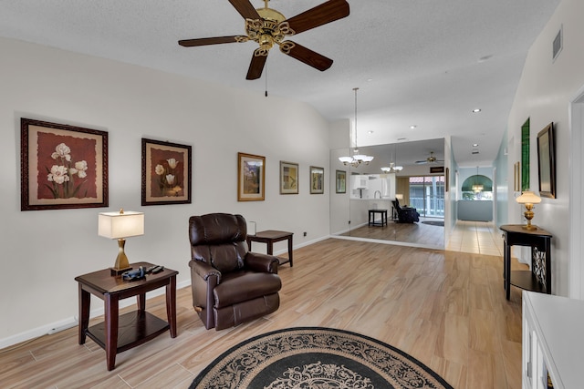 sitting room with ceiling fan with notable chandelier, a textured ceiling, and light wood-type flooring