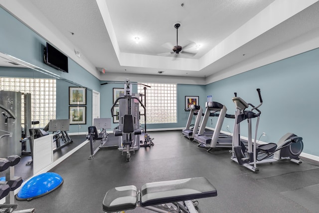 exercise room with ceiling fan, plenty of natural light, and a tray ceiling