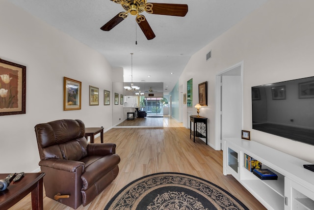 living room with light hardwood / wood-style floors, lofted ceiling, a textured ceiling, ceiling fan with notable chandelier, and built in shelves