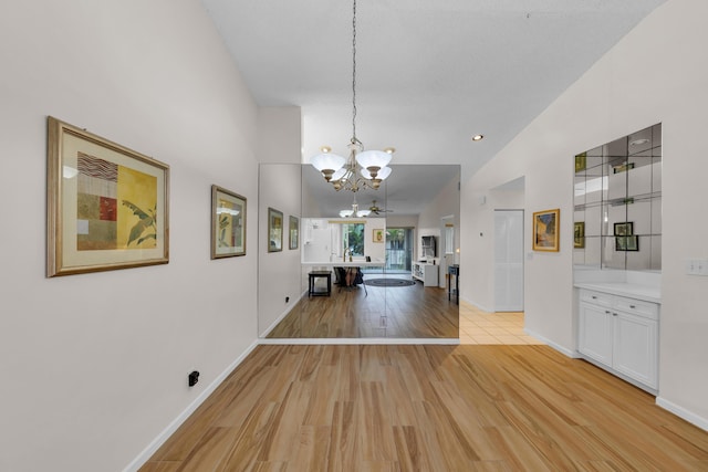 unfurnished dining area with ceiling fan with notable chandelier, vaulted ceiling, and light wood-type flooring