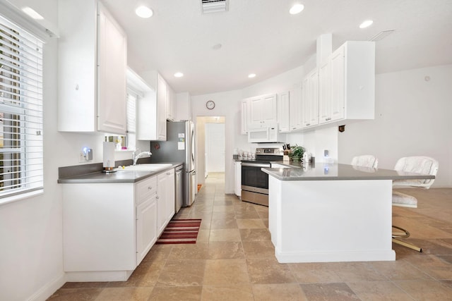 kitchen with electric stove, dishwashing machine, white cabinetry, a kitchen breakfast bar, and kitchen peninsula