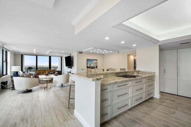 kitchen featuring white cabinetry, light hardwood / wood-style floors, black electric cooktop, light stone countertops, and a breakfast bar