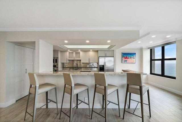 kitchen with tasteful backsplash, crown molding, appliances with stainless steel finishes, a water view, and light stone counters