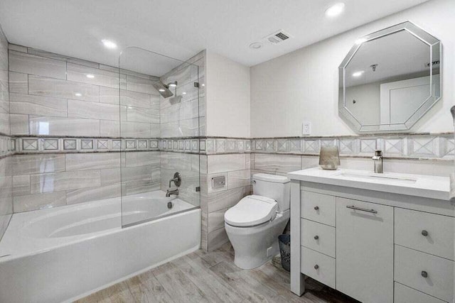 full bathroom featuring hardwood / wood-style floors, tiled shower / bath combo, vanity, tile walls, and toilet