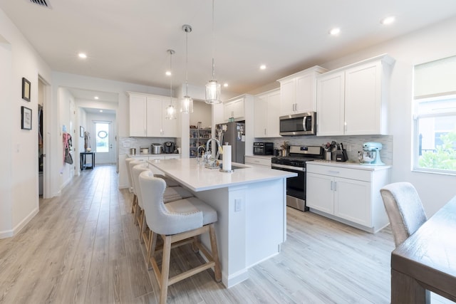 kitchen featuring decorative light fixtures, a center island with sink, sink, white cabinetry, and stainless steel appliances